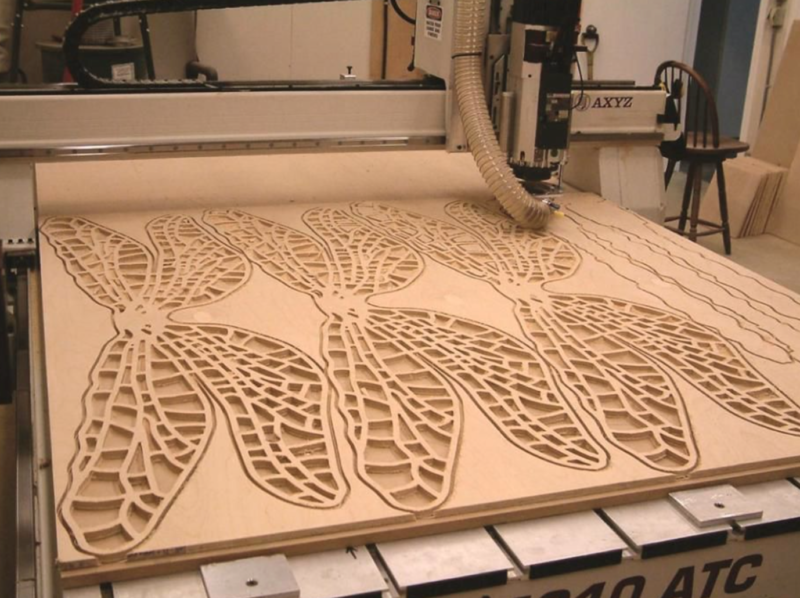CNC machine cutting intricate insect wing patterns in wood