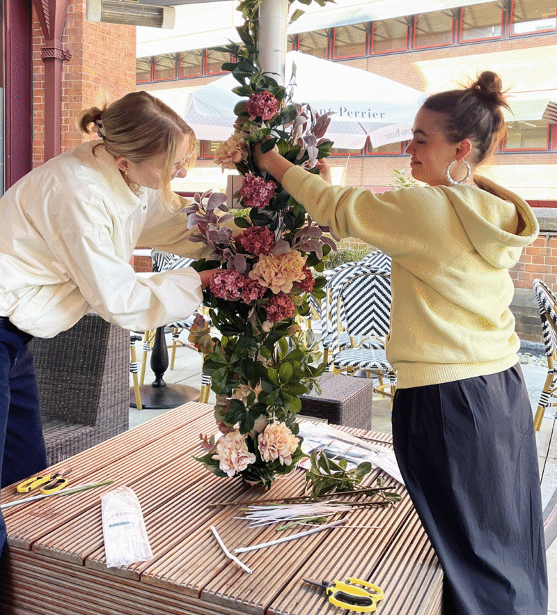 Two women arranging tall floral centerpiece